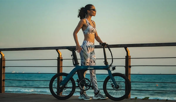 Une femme pousse un vélo électrique Fiido X pour une promenade sur la plage.