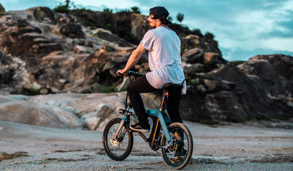 Un cycliste sur le Fiido D11 explorant un terrain côtier rocheux au coucher du soleil