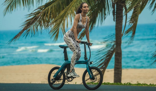 Une femme en forme conduit un vélo électrique Fiido D11 sur la plage.