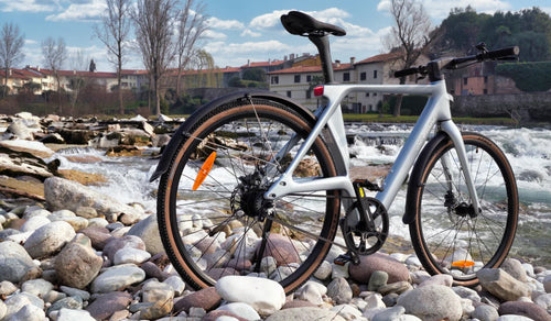 Vélo électrique ultraléger en fibre de carbone Fiido Air présenté sur une berge rocheuse au bord d’une eau vive.