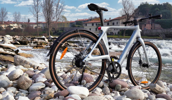 Vélo électrique ultraléger en fibre de carbone Fiido Air présenté sur une berge rocheuse au bord d’une eau vive.