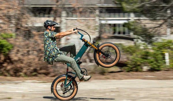 Un cycliste réalise une roue arrière sur un vélo électrique à pneus larges Fiido M1 Pro, mettant en valeur son cadre pliant compact, ses pneus larges et sa suspension avant sur une route urbaine.